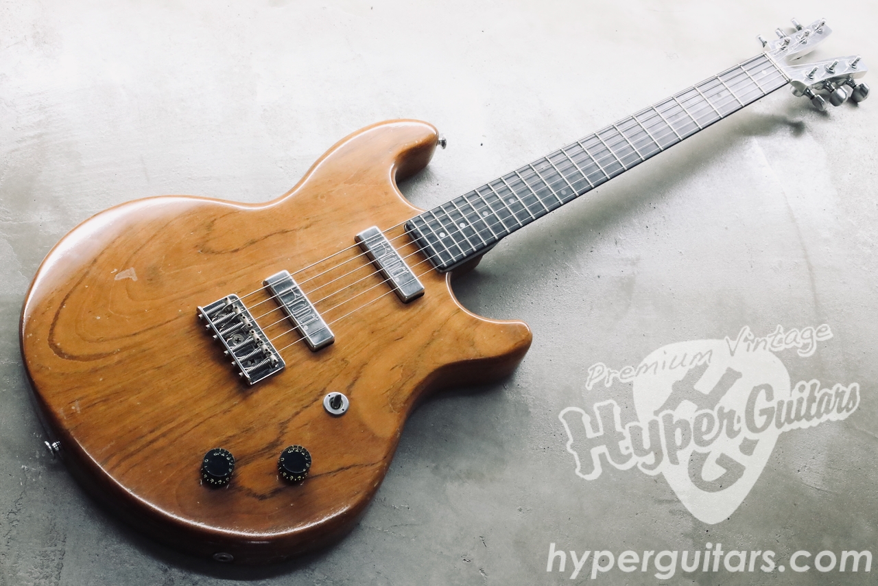 Natural finish electric guitar with two humbucker pickups and a fixed bridge lying on a concrete floor, watermark visible in the corner.