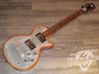 Orange-edged vintage electric guitar with engraved metal body and two pickups resting on a wooden floor. (HyperGuitars watermark visible)
