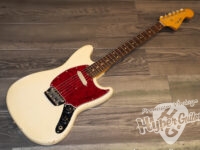 Cream Fender-style electric guitar with a red pickguard resting on a wooden floor.